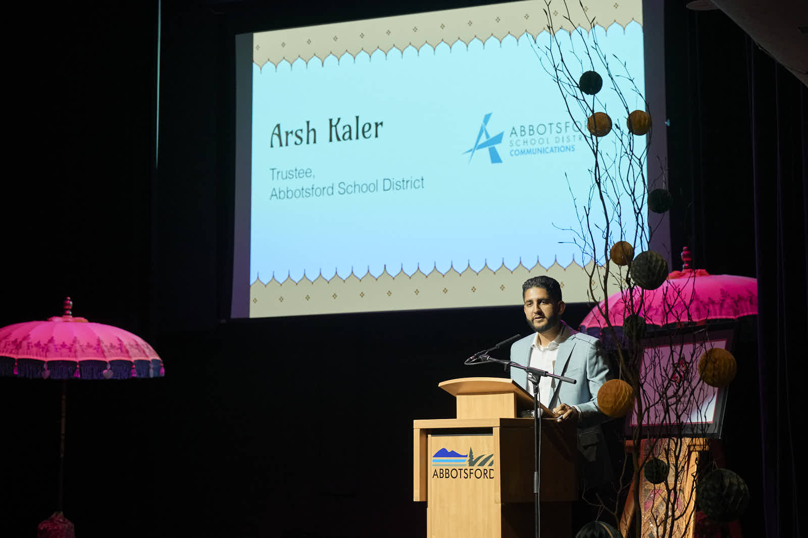Arsh Kaler speaking at a podium, introduced as Trustee, Abbotsford School District